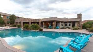 A swimming pool with lounge chairs, a stone building with a flat roof, and a clear sky.