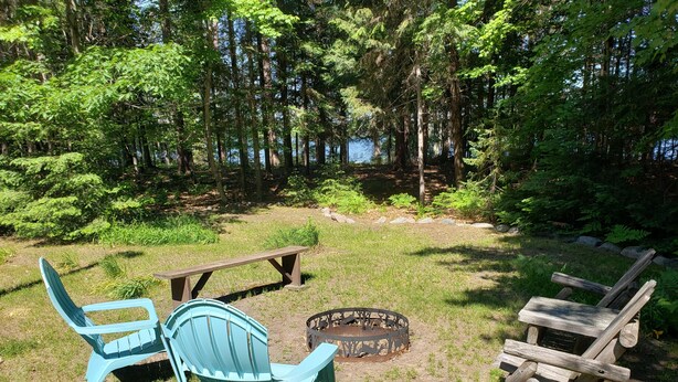 A picnic area with a fire pit, two Adirondack chairs, and a wooden bench. - Peace, Privacy and a Pontoon!! No steps in home or to water! (Eagle River)