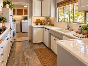 A modern kitchen with white cabinetry, a built-in oven, a coffee maker, and a window with a view of trees.