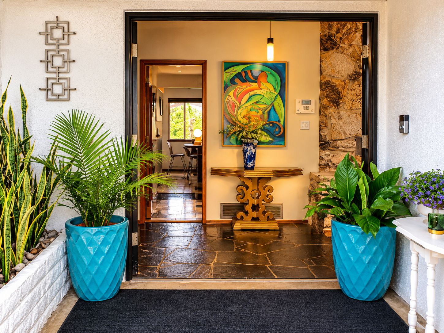 A hotel entrance with a stone wall, a colorful abstract painting, and large potted plants.