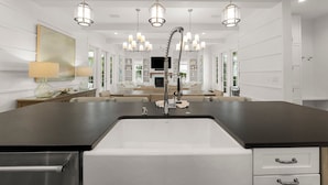 Une cuisine moderne dotée d’un grand îlot central, d’appareils électroménagers en acier inoxydable et de luminaires suspendus.