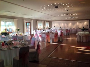 Un salón de banquetes con mesas redondas, sillas y un elegante candelabro.