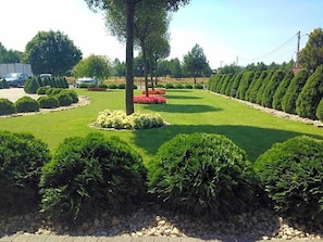 A well-maintained garden with neatly trimmed hedges, a central circular flower bed, and a row of trees on one side.