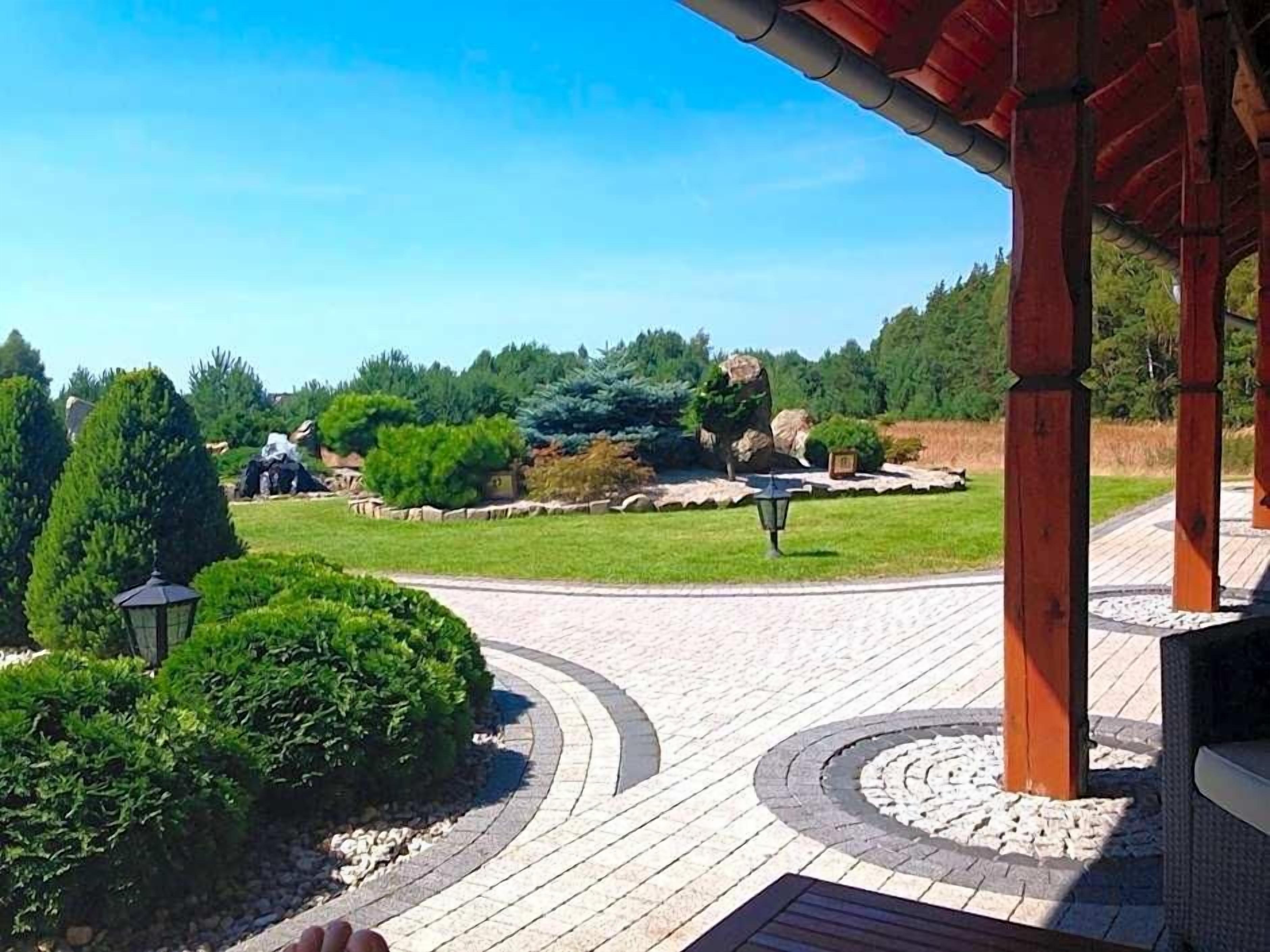 A paved pathway leading to a gazebo with a view of a landscaped garden and distant buildings.