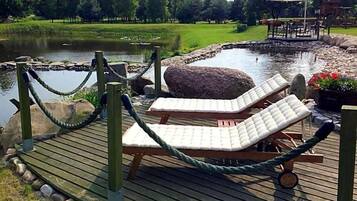 A wooden deck with lounge chairs and a rope barrier near a pond.