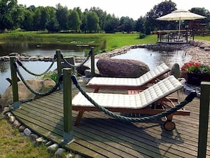 A wooden deck with lounge chairs and a rope barrier near a pond.