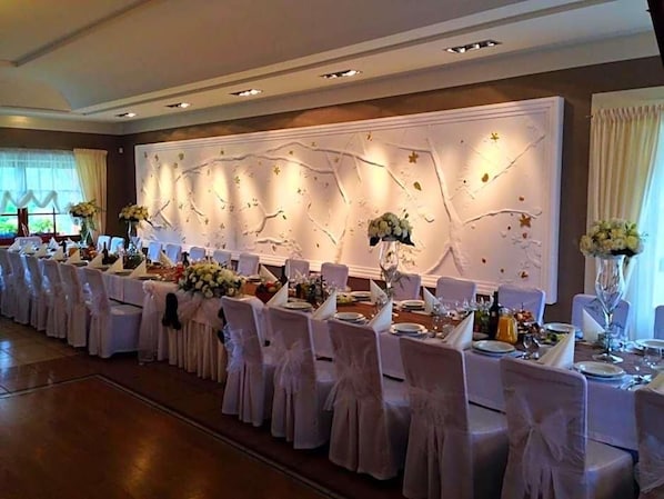 A banquet hall with long tables set for a formal event, decorated with floral arrangements and white tablecloths.