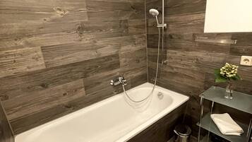 Un baño moderno con una bañera independiente, paneles de madera en la pared, un estante de vidrio con artículos de aseo y un pequeño cubo de basura.