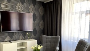 Een moderne woonkamer met een flatscreen televisie, een grijze fauteuil, een witte console tafel en een glazen salontafel.