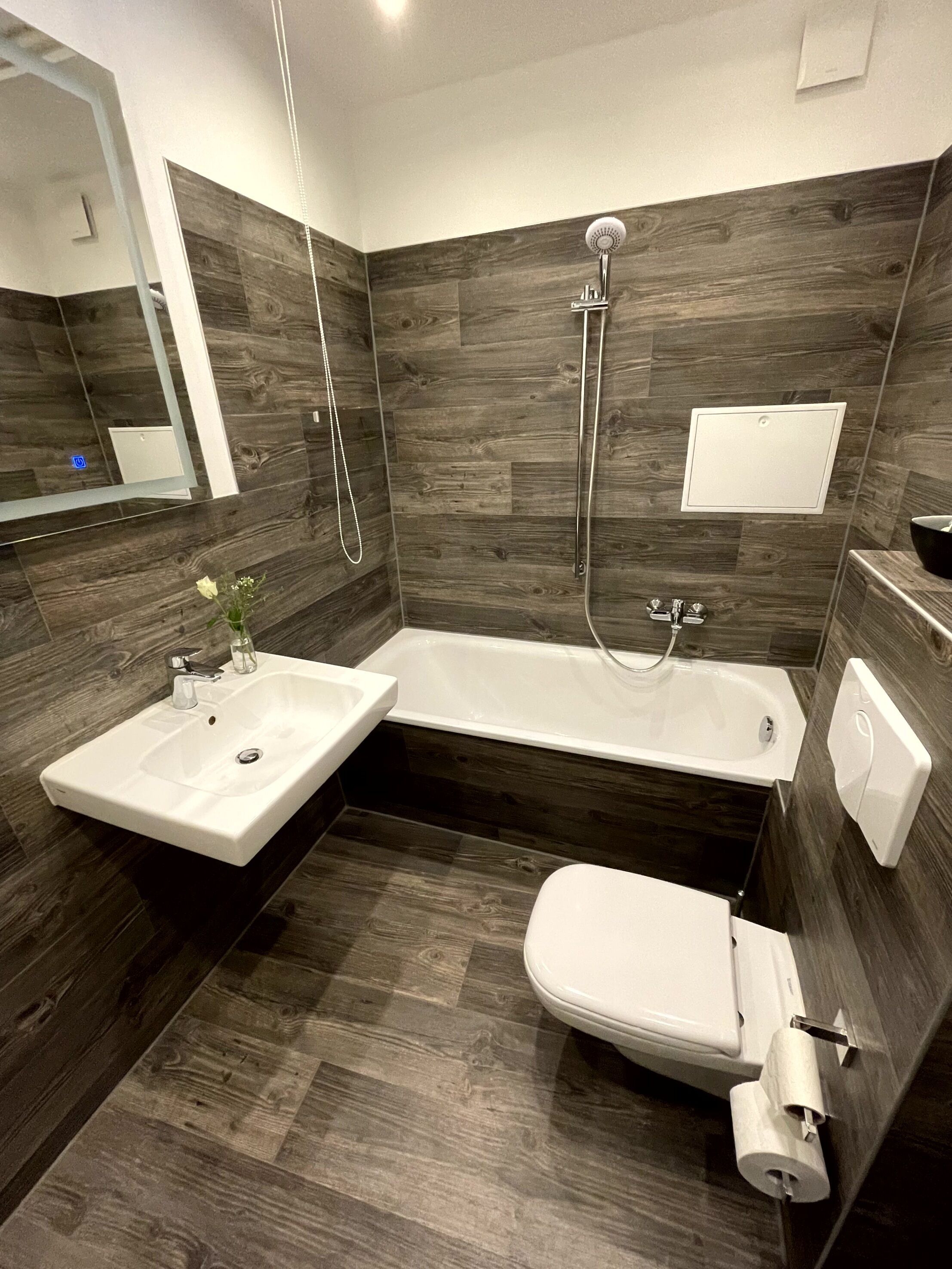 A modern bathroom with a corner sink, a bathtub, and a toilet.