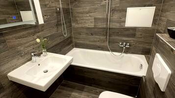 A modern bathroom with a corner sink, a bathtub, and a toilet.