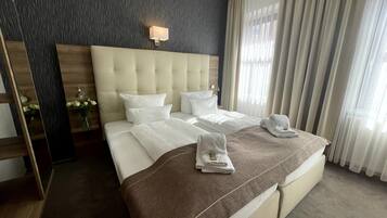 Habitación de hotel con una cama grande, un cabecero, una mesita de noche con lámpara y una ventana con cortinas.