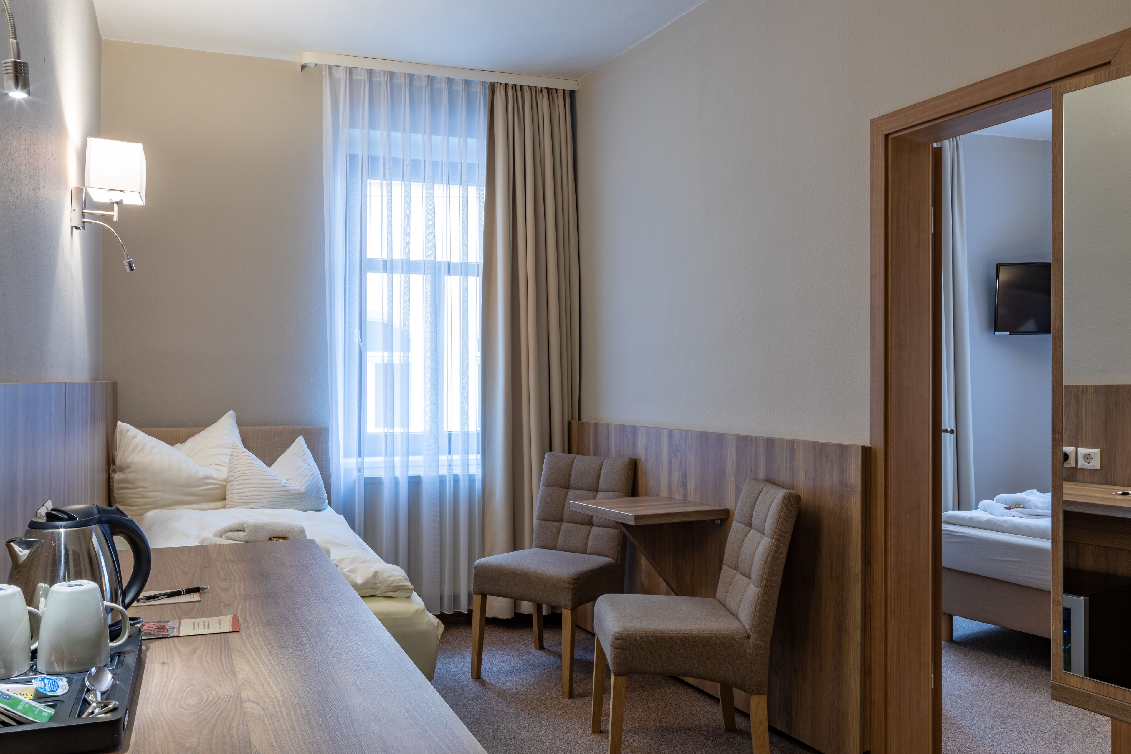A hotel room with a bed, a desk, two chairs, a coffee maker, and a TV.