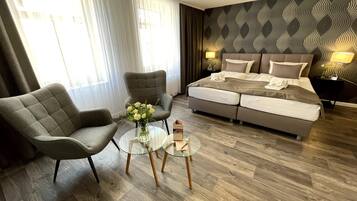 Ein modernes Hotelzimmer mit einem großen Bett, zwei Sesseln, einem Glastisch und einer Wand mit Muster.