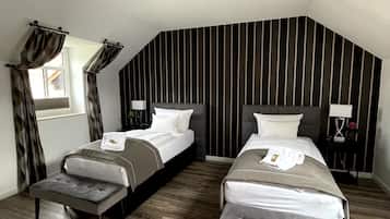 A modern bedroom with two beds, a bench, a window with curtains, a wall-mounted light, and a striped wall design.