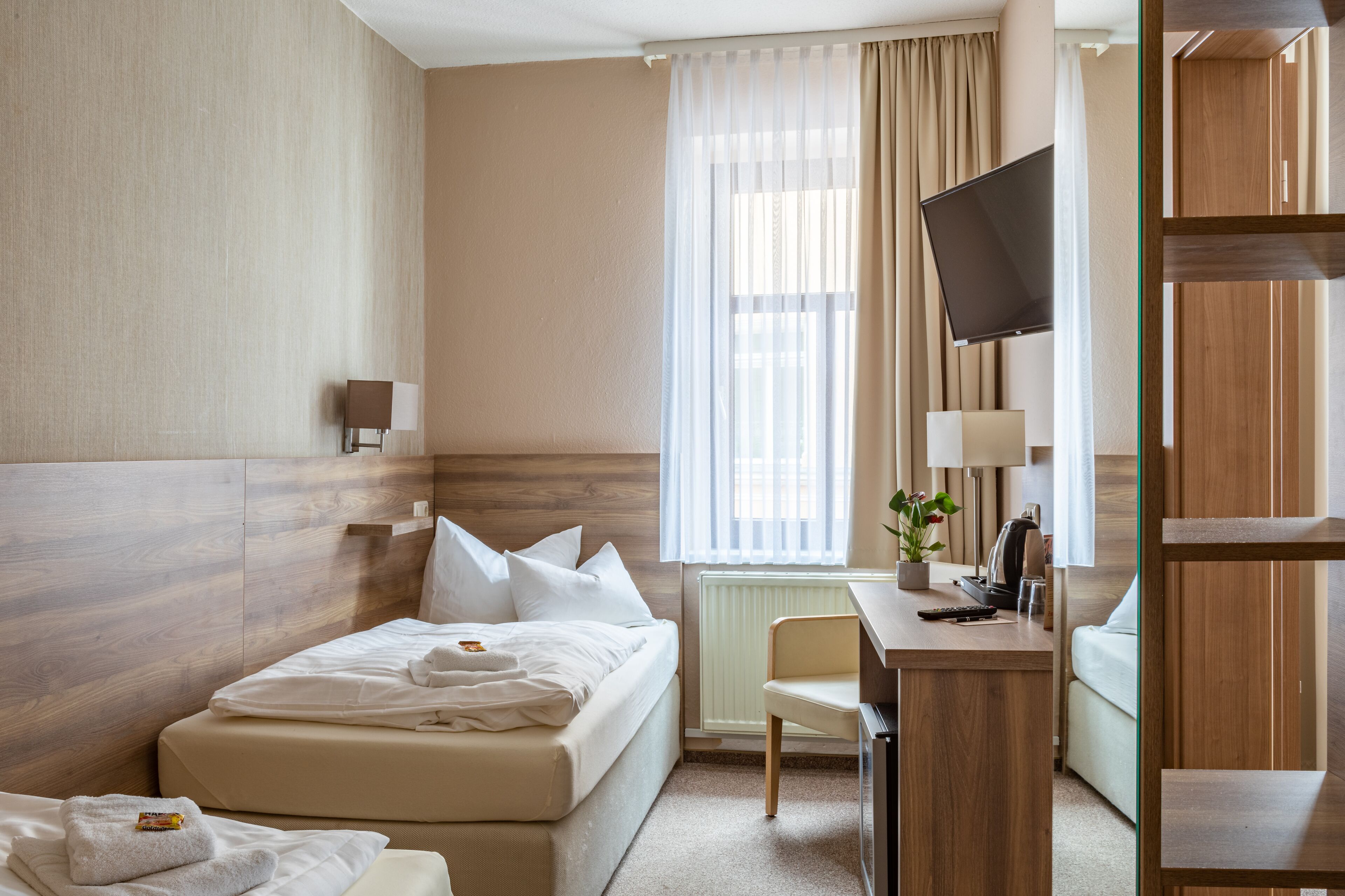 Ein Hotelzimmer mit Bett, Schreibtisch, Stuhl, Fernseher und einem Fenster mit Vorhängen.
