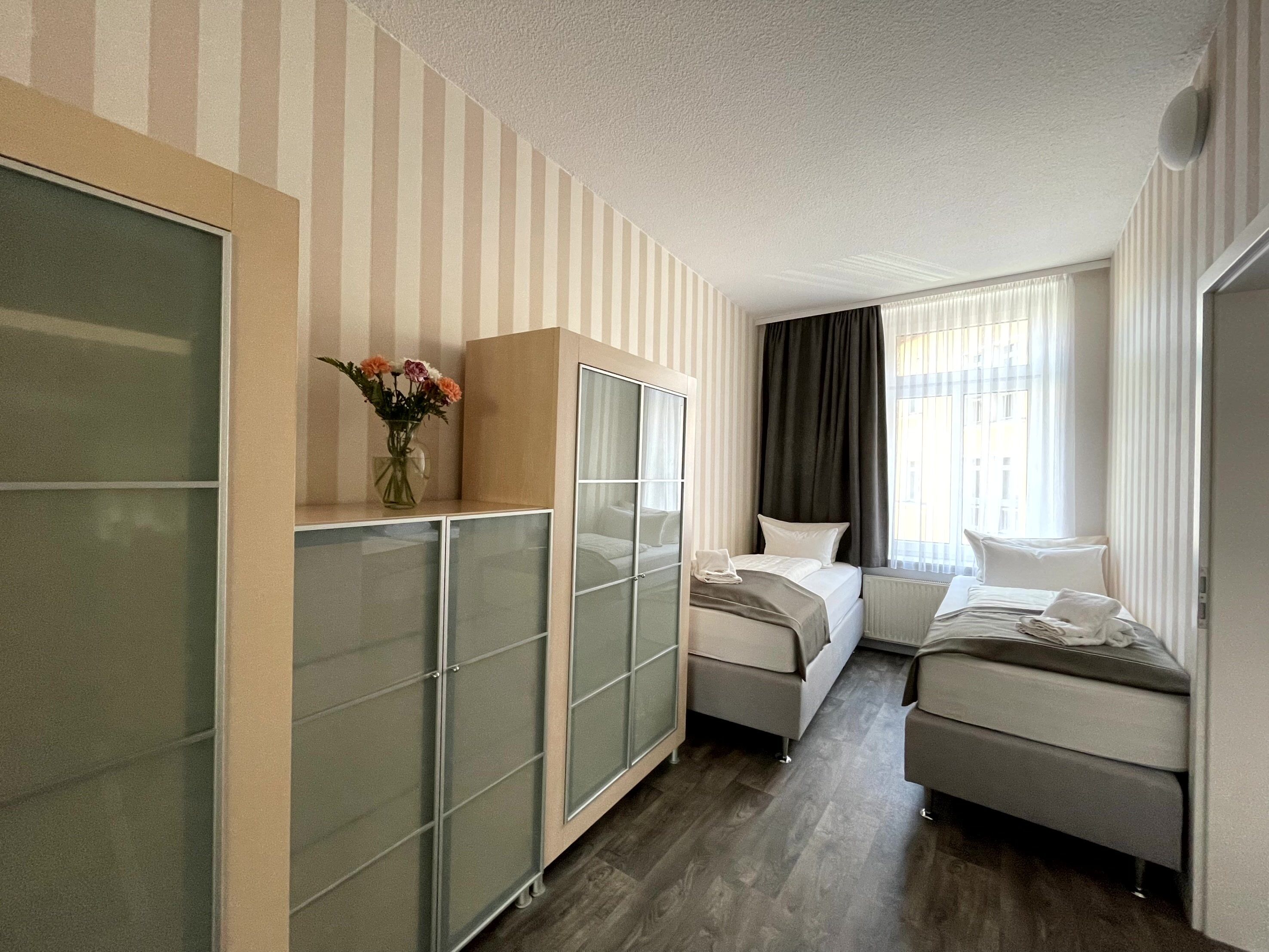 Una habitación de hotel con cama, sofá, armario y ventana con cortinas.