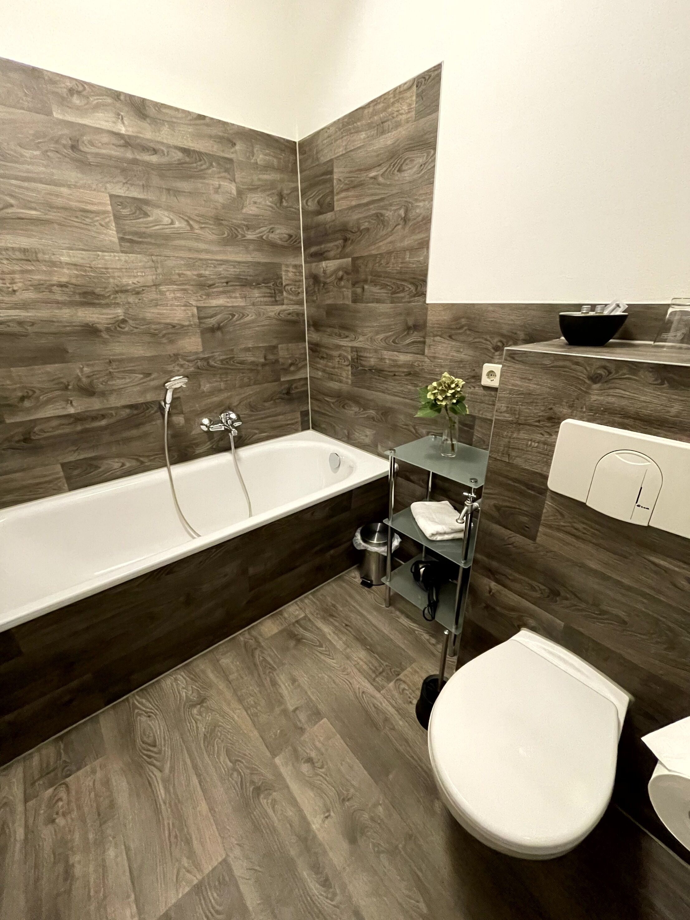 A modern bathroom with a wooden wall panel design, a bathtub, a toilet, and a small sink area.