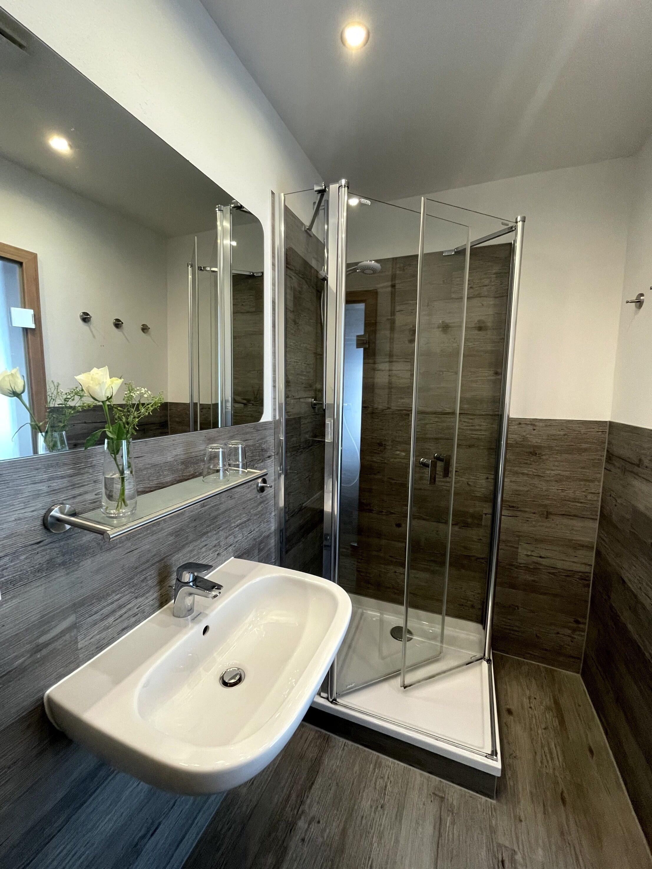 A modern bathroom with a glass-enclosed shower, a white sink, and a large mirror.
