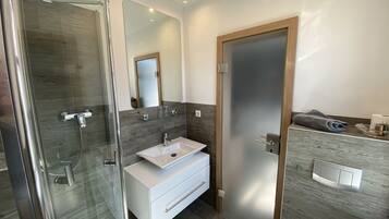 Un baño moderno con cabina de ducha de vidrio, tocador blanco con lavamanos y puerta de madera.