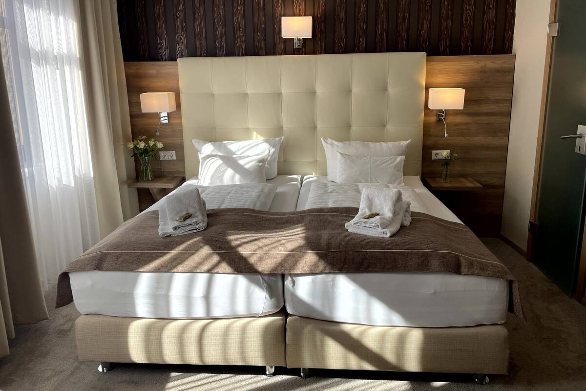 A hotel room with a large bed, two bedside lamps, a wooden headboard, and a nightstand with a vase of flowers.