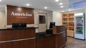 Un espace d’accueil avec un comptoir de réception en bois, une enseigne indiquant « AmerInn by Wyndham », un réfrigérateur rempli de boissons et une étagère avec des en-cas.