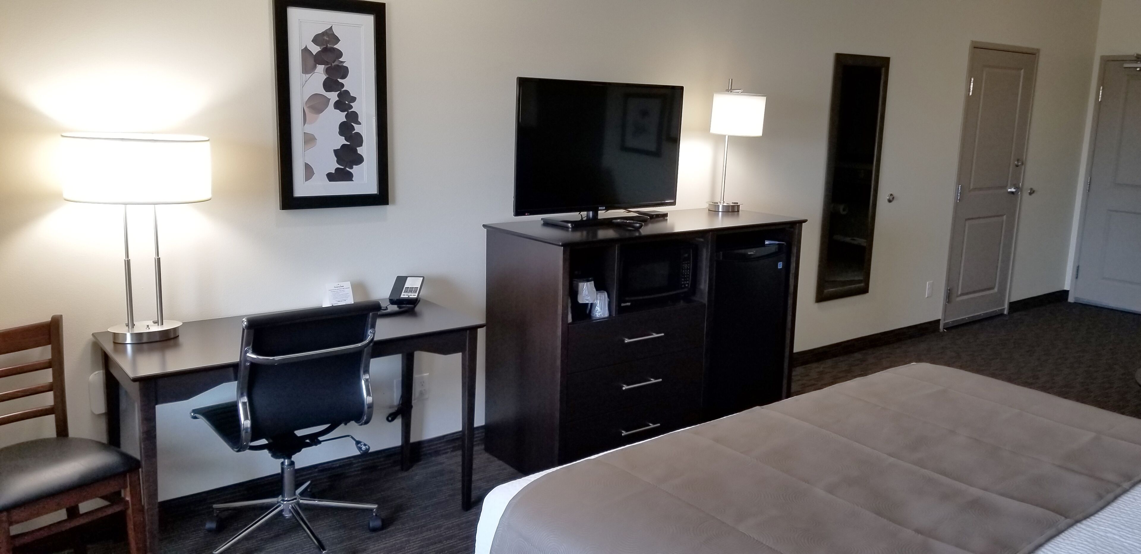Habitación de hotel con cama, escritorio con silla, televisor, cómoda y lámpara.