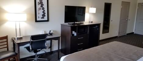 Habitación de hotel con cama, escritorio con silla, televisor, cómoda y lámpara.