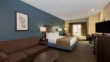 A hotel room with a bed, a sofa, a desk, a TV, and a framed picture on the wall.