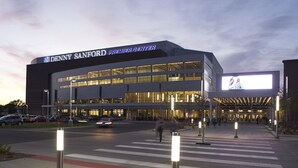 Un bâtiment moderne avec une grande enseigne lumineuse sur laquelle on peut lire : « Denny Sanford Premier Center ».