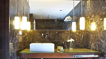 A bathroom with a marble wall, a sink with a mirror, and a towel rack.