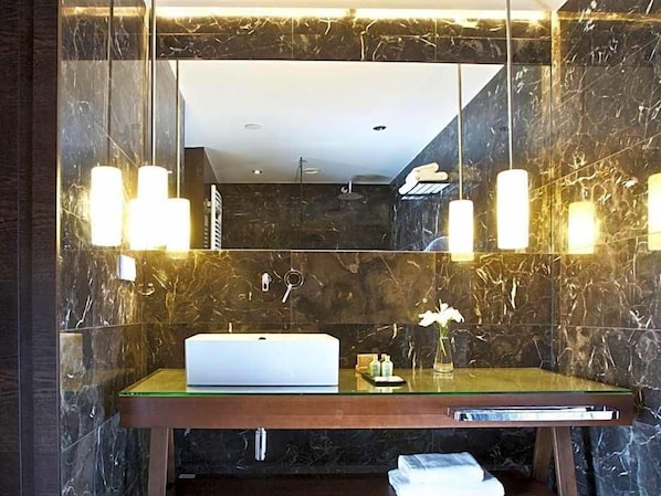 A bathroom with a marble wall, a sink with a mirror, and a towel rack.