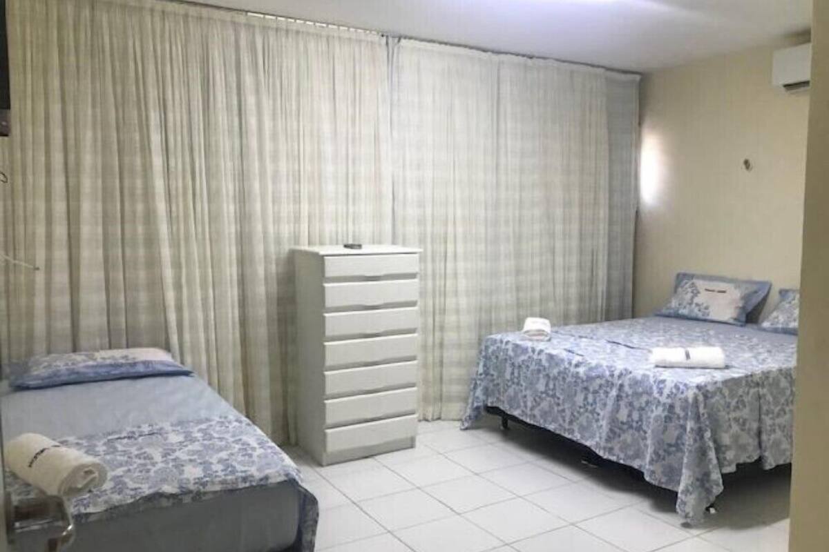 Quarto com duas camas, cômoda e cortina.