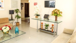 A modern living room with a glass coffee table, a sofa, a TV mounted on the wall, and various decorative items including plants and figurines. - Hospedaria Gebel LocDay (Recife)