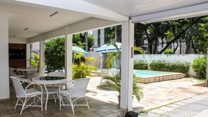 A covered outdoor area with a pool, white wicker furniture, and umbrellas. - Hospedaria Gebel LocDay (Recife)