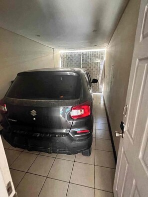 A narrow hallway with a parked car and a door on the right. - Casa Caballito (León)