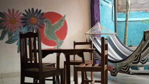 A room with a mural of a bird and flowers, a hammock, and wooden chairs. - Casa Caballito (León)