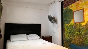 A bedroom with a bed, a nightstand, a wall-mounted fan, and a mural on the wall. - Casa Caballito (León)