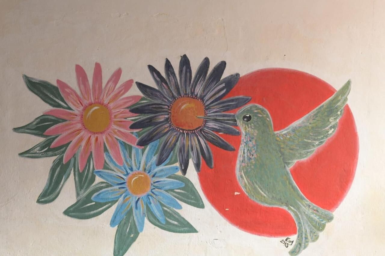 A painting of a hummingbird near flowers with a red background.