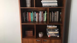 A wooden bookshelf with multiple shelves containing various books and a decorative vase. - Sunny Holiday Home Near the Beach (Tauranga)