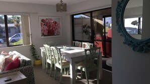 A dining area with a white table and chairs, a large window with a view of the outside, and a mirror on the wall. - Sunny Holiday Home Near the Beach (Tauranga)