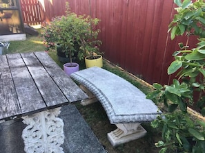 Uma mesa de madeira rústica com um banco, rodeada por plantas em vasos e um cercado de madeira vermelha.