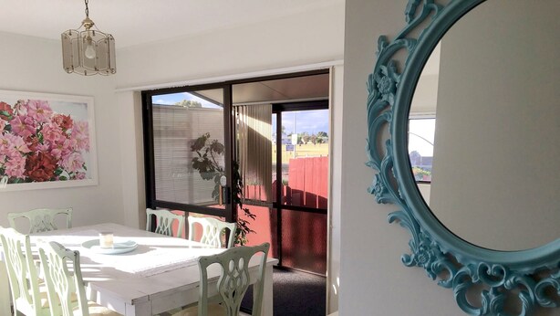 A dining area with a white table and chairs, a large floral painting, and a blue ornate mirror. - Sunny Holiday Home Near the Beach (Tauranga)