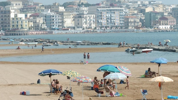 A beach with people sunbathing, umbrellas, and boats in the water. - Corso Messina (Crotone)