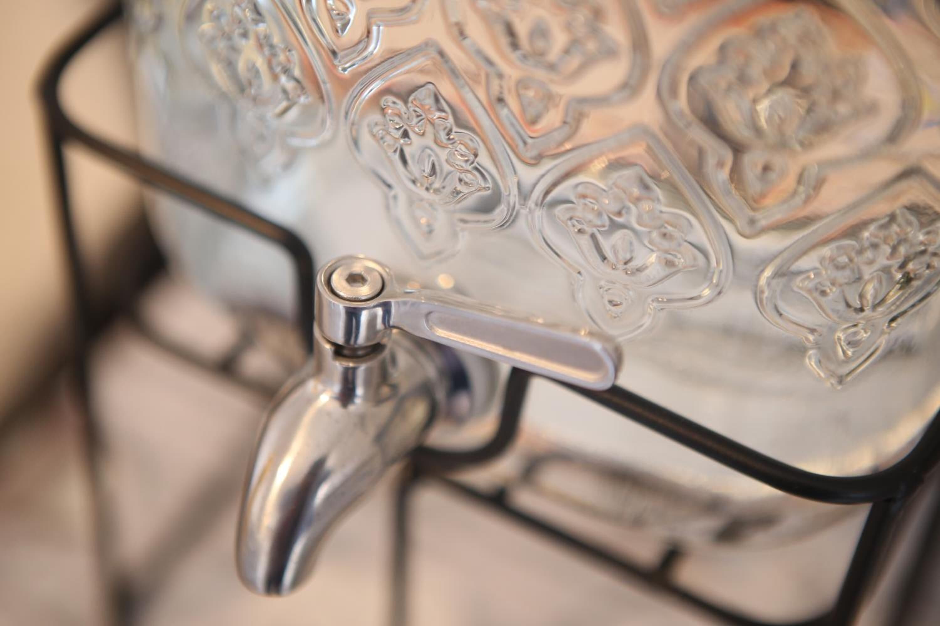 A metallic faucet attached to a glass container with embossed floral patterns.