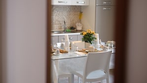 A kitchen with white cabinets, a tiled backsplash, and a dining table set with white chairs. - Corso Messina (Crotone)