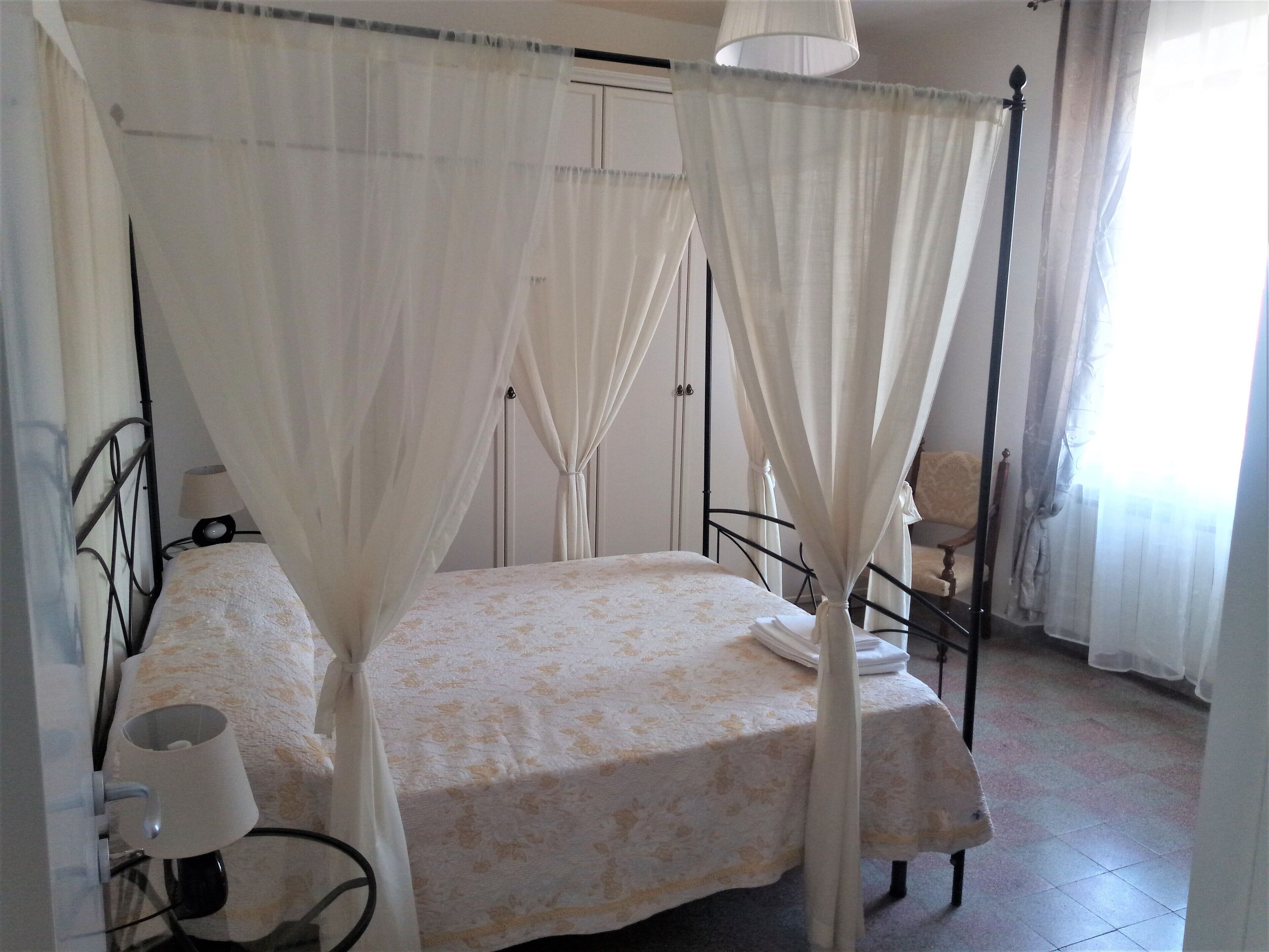 A bedroom with a four-poster bed, a bedside table, a lamp, and a chair.