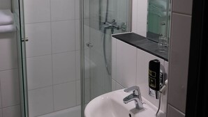 A glass-enclosed shower stall with a handheld showerhead, a white sink with a chrome faucet, and a towel rack. - Minx - Cityhotels (Aachen)