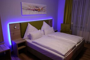 Ein ordentlich bezogenes Bett mit weißen Laken, einem grünen Kopfteil und einem Nachttisch mit Lampe.
