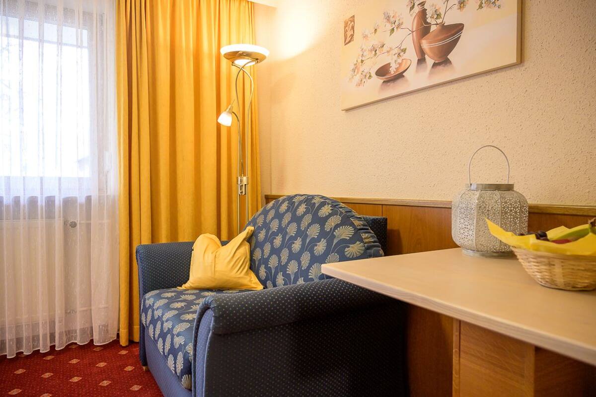 A room with a sofa, a table, a lamp, a vase, and a painting on the wall.